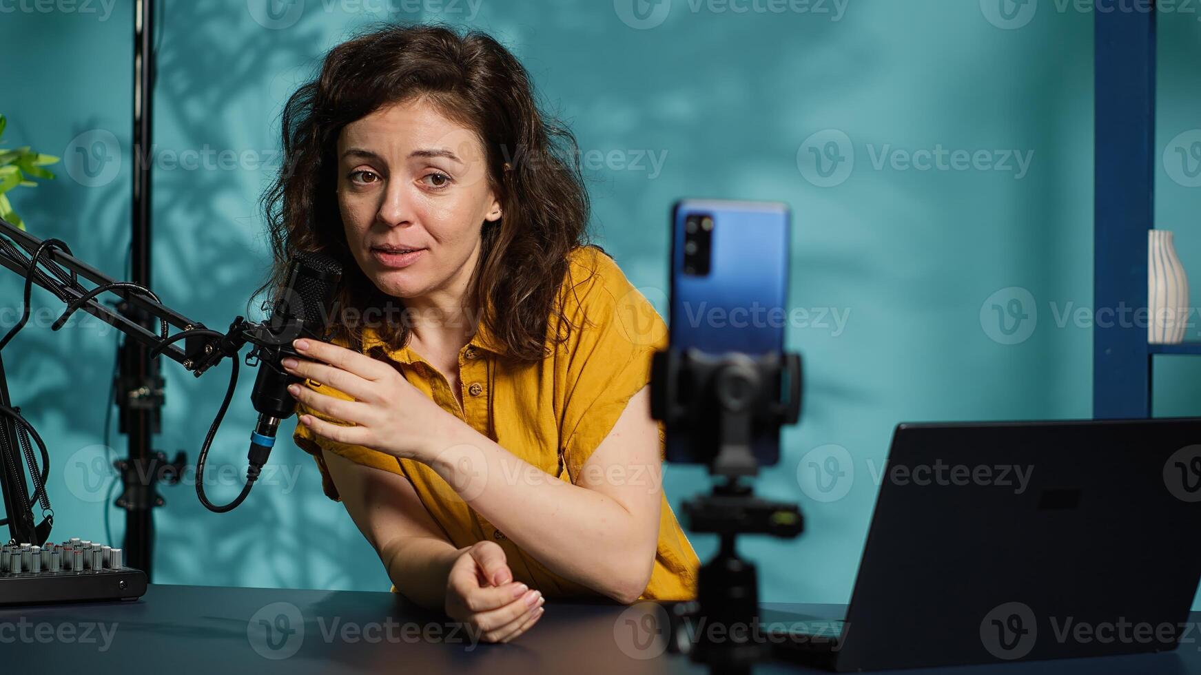 Influencer in home studio using smartphone on phone holder to record live broadcast, greeting subscribers. Internet star hosts q and a session with viewers using cellphone, camera A photo