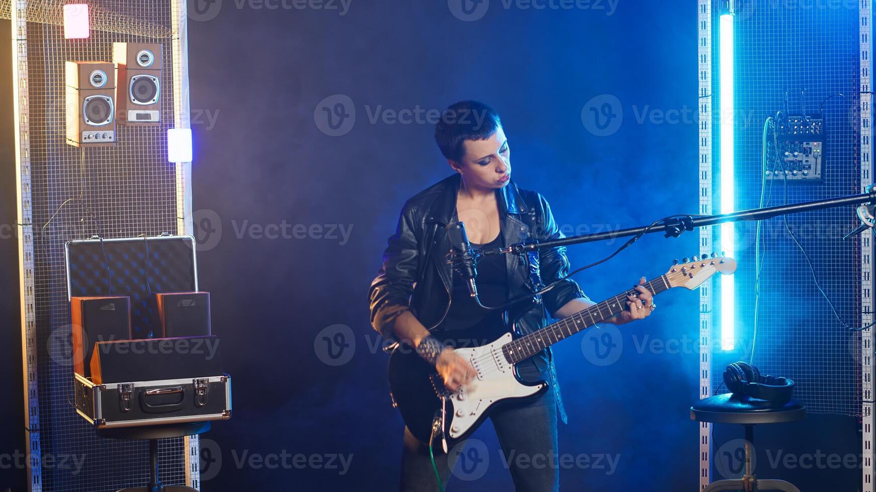 Talented female musician playing guitar with confidence in a dark urban studio. Rebellious woman rocker with an edgy spirit and bold style creating a great fierce performance. Camera B. photo