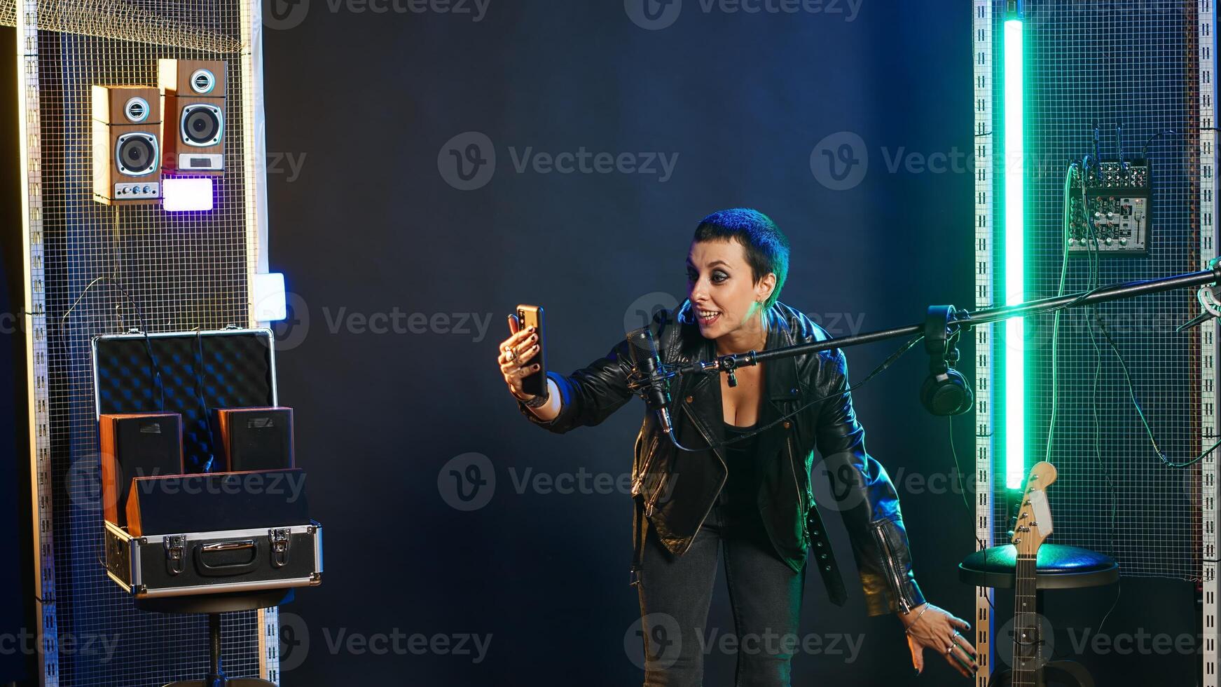 Rocker singer chatting on a call and showing the studio on a selfie camera, smartphone user recording her singing session. Cool edgy artist on live chat having a conversation. Camera B. photo
