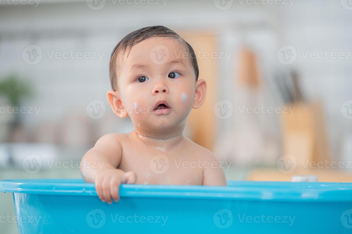 Happy toddler enjoying a playful bath in a blue tub at home during the afternoon photo