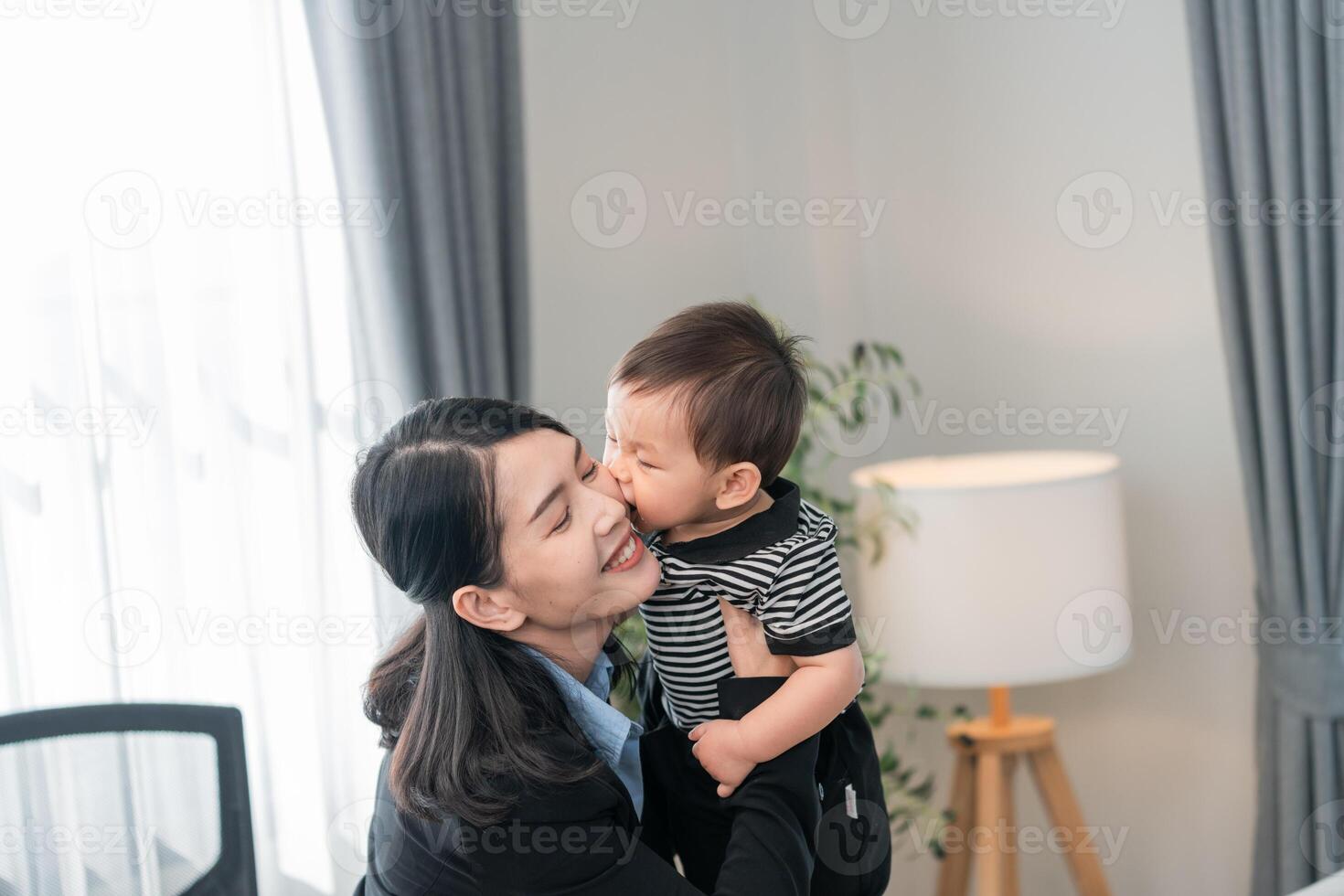 Woman joyfully embraces a toddler in a bright, modern home office during the daytime, capturing a moment of love and connection photo