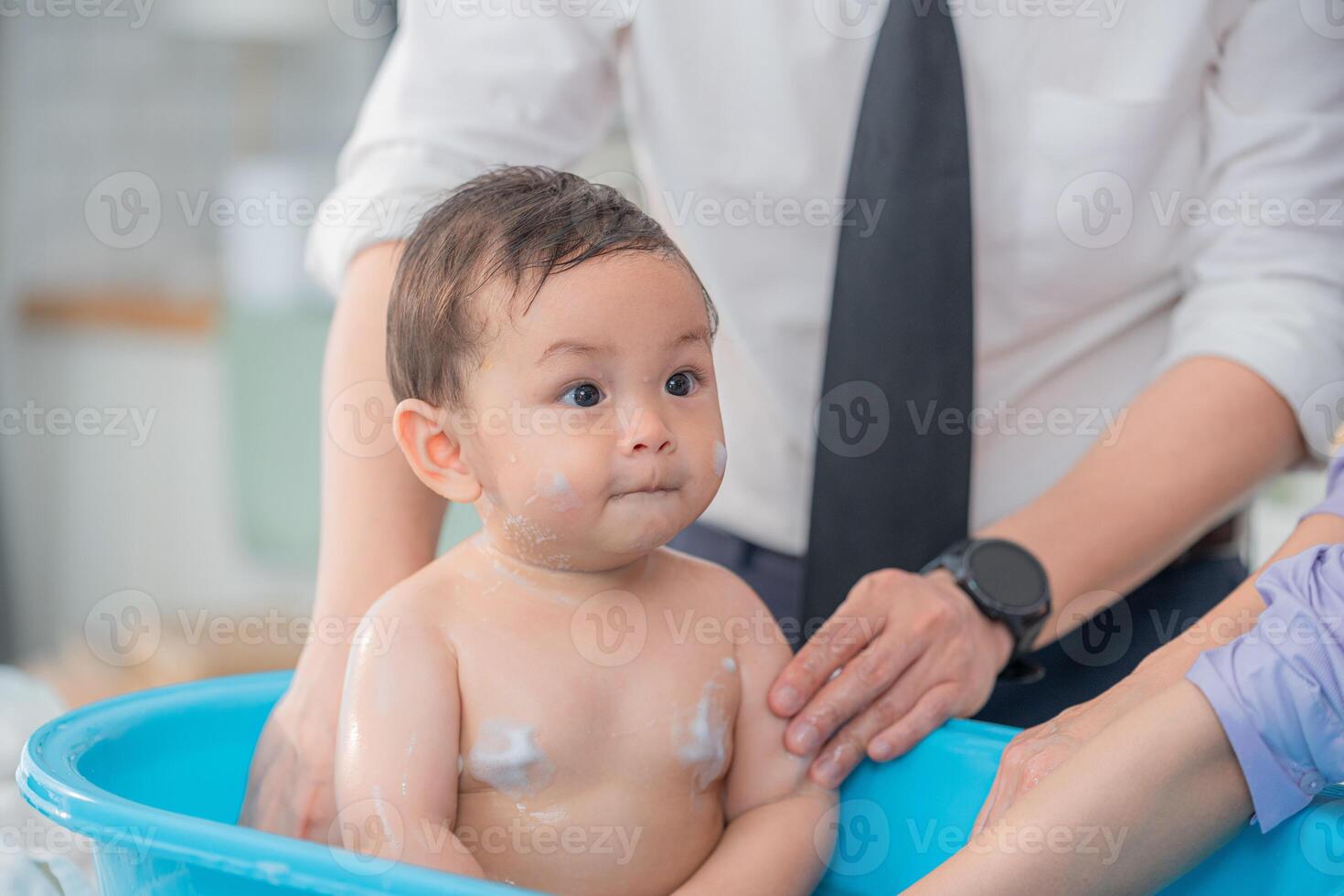 Baby enjoying a bath while caregivers assist in a bright and modern bathroom setting photo