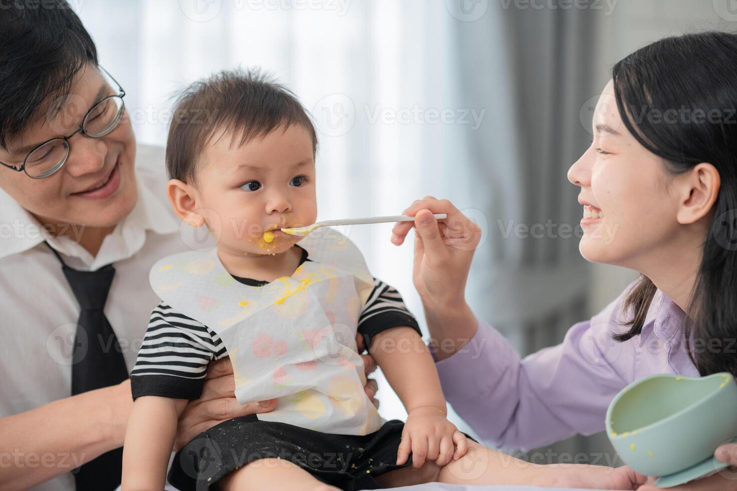 Parents feeding their toddler during a joyful mealtime at home in a bright, cozy kitchen setting photo