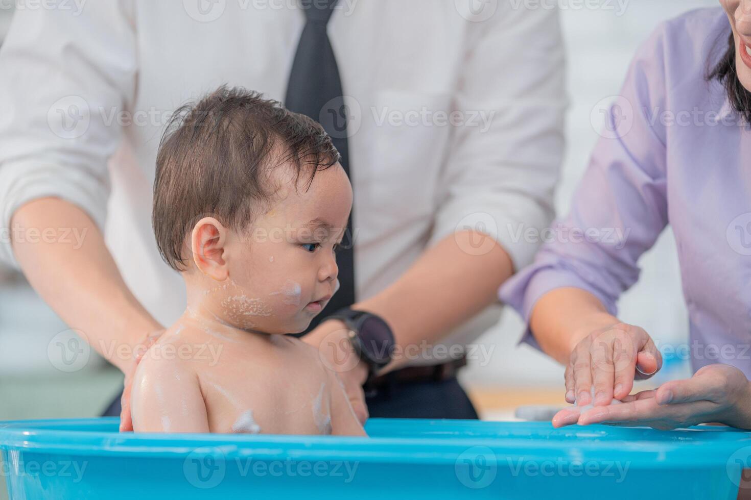Toddler enjoying a bath with attentive adults in a bright, modern bathroom setting during daytime photo