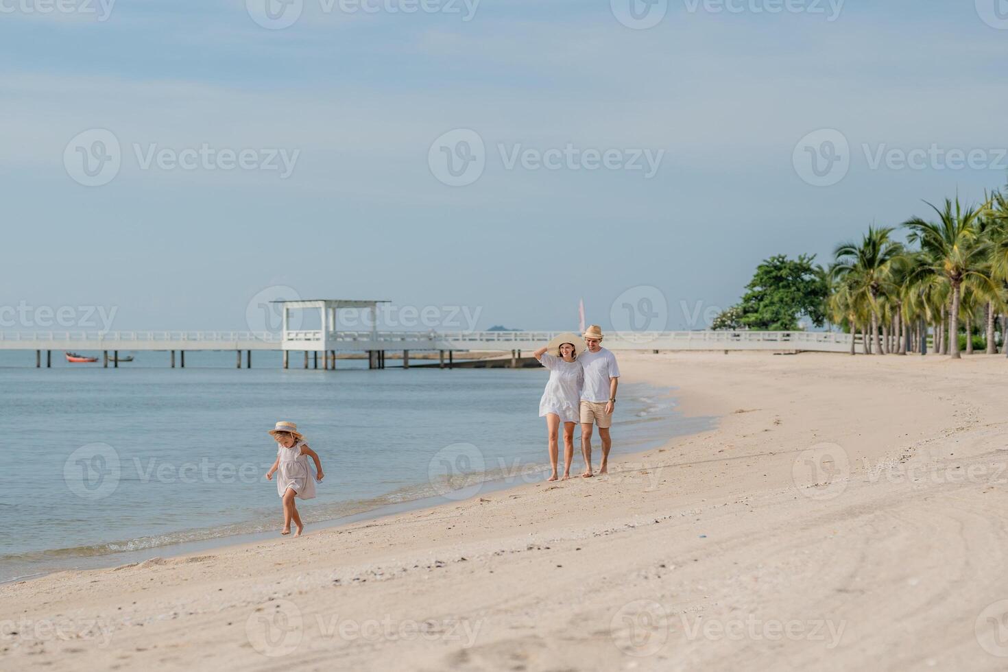 Family enjoys a sunny day walking along a tranquil beach with palm trees and a pier in the distance photo