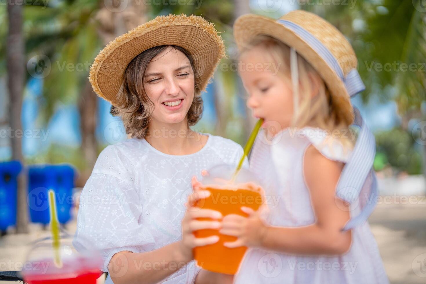 Relaxing day at the beach with mother and daughter enjoying refreshing drinks under palm trees photo