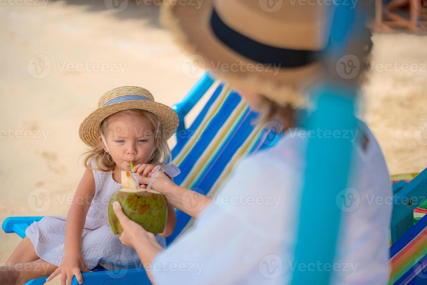 Young girl enjoys coconut drink while relaxing on beach chair in tropical setting photo
