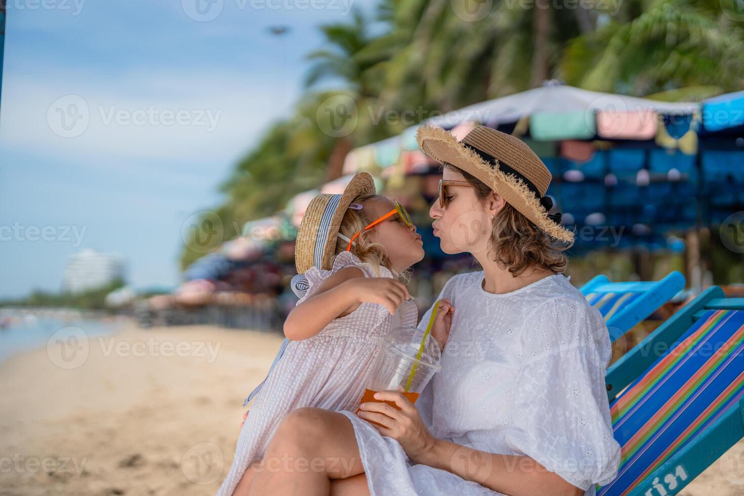 Mother and daughter enjoying a sunny beach day while sipping drinks in vibrant tropical surroundings photo