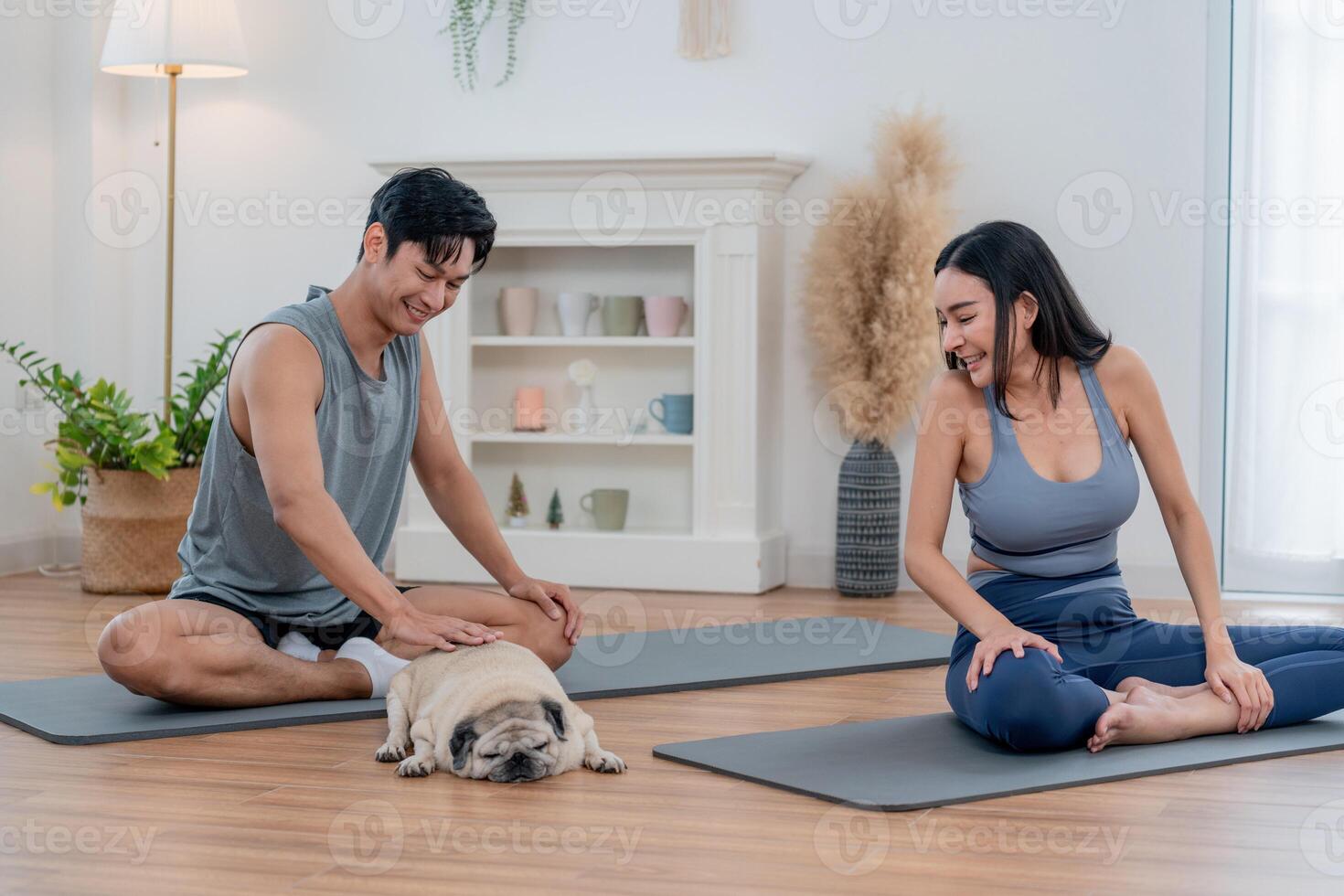 Couple enjoys yoga session at home with their playful pug in a cozy living room photo
