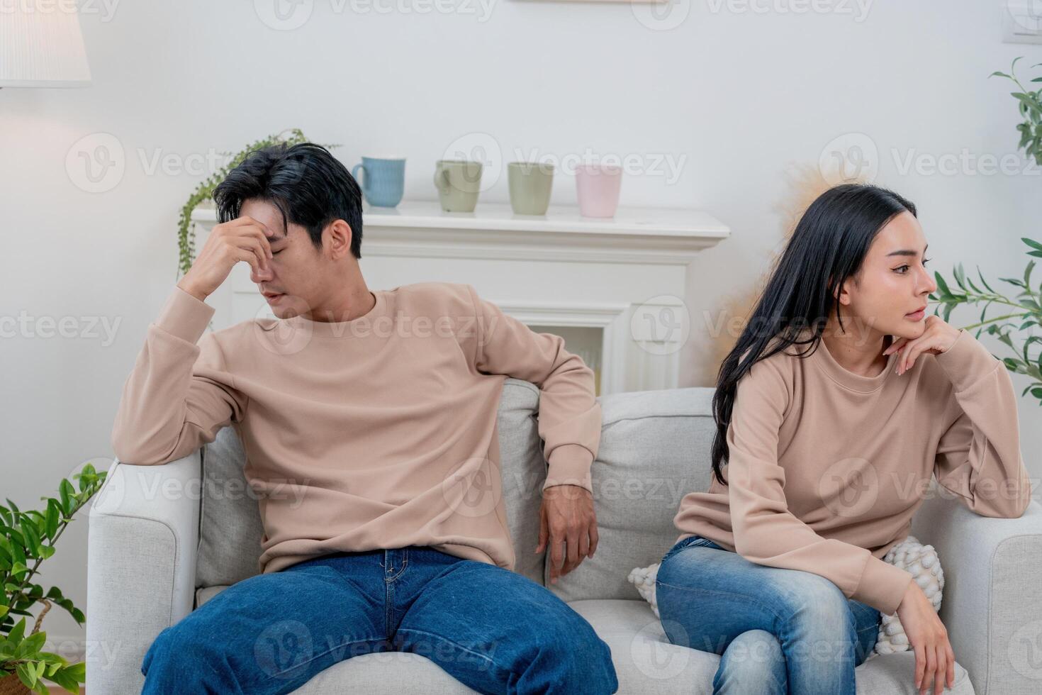 Couple sitting apart on a couch in a living room after an argument in soft lighting photo