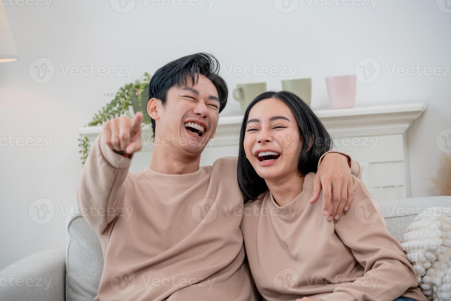 Joyful couple sharing laughter while relaxing on a cozy sofa at home during a sunny afternoon photo