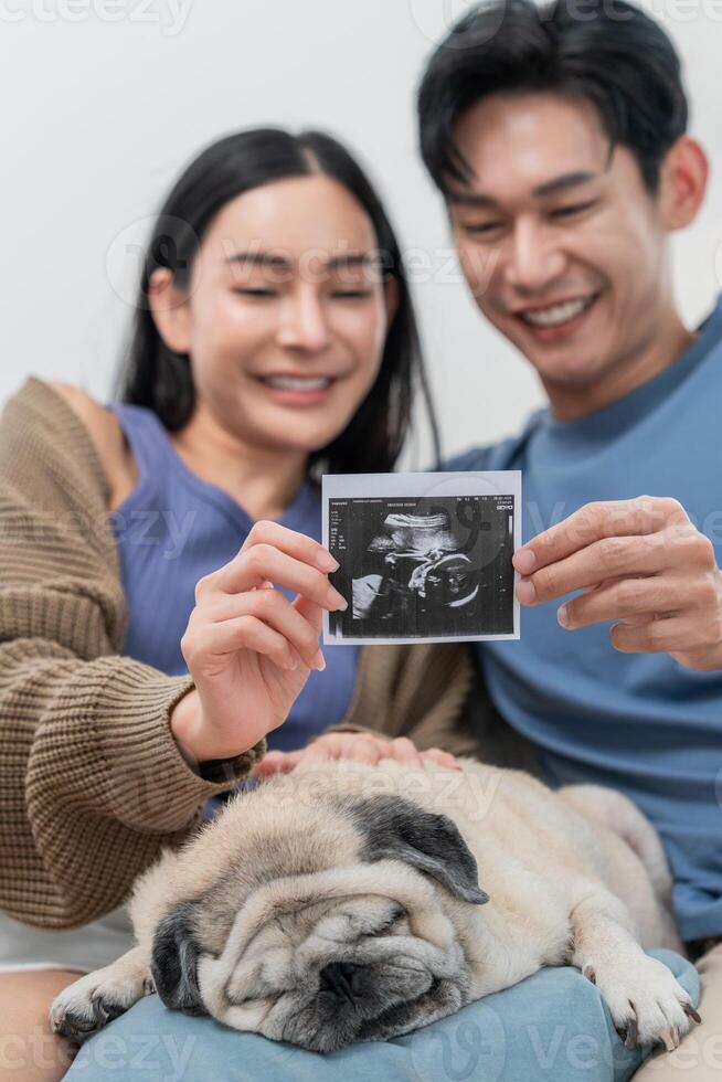 Excited couple shares ultrasound image while sitting on a couch with their sleeping dog photo