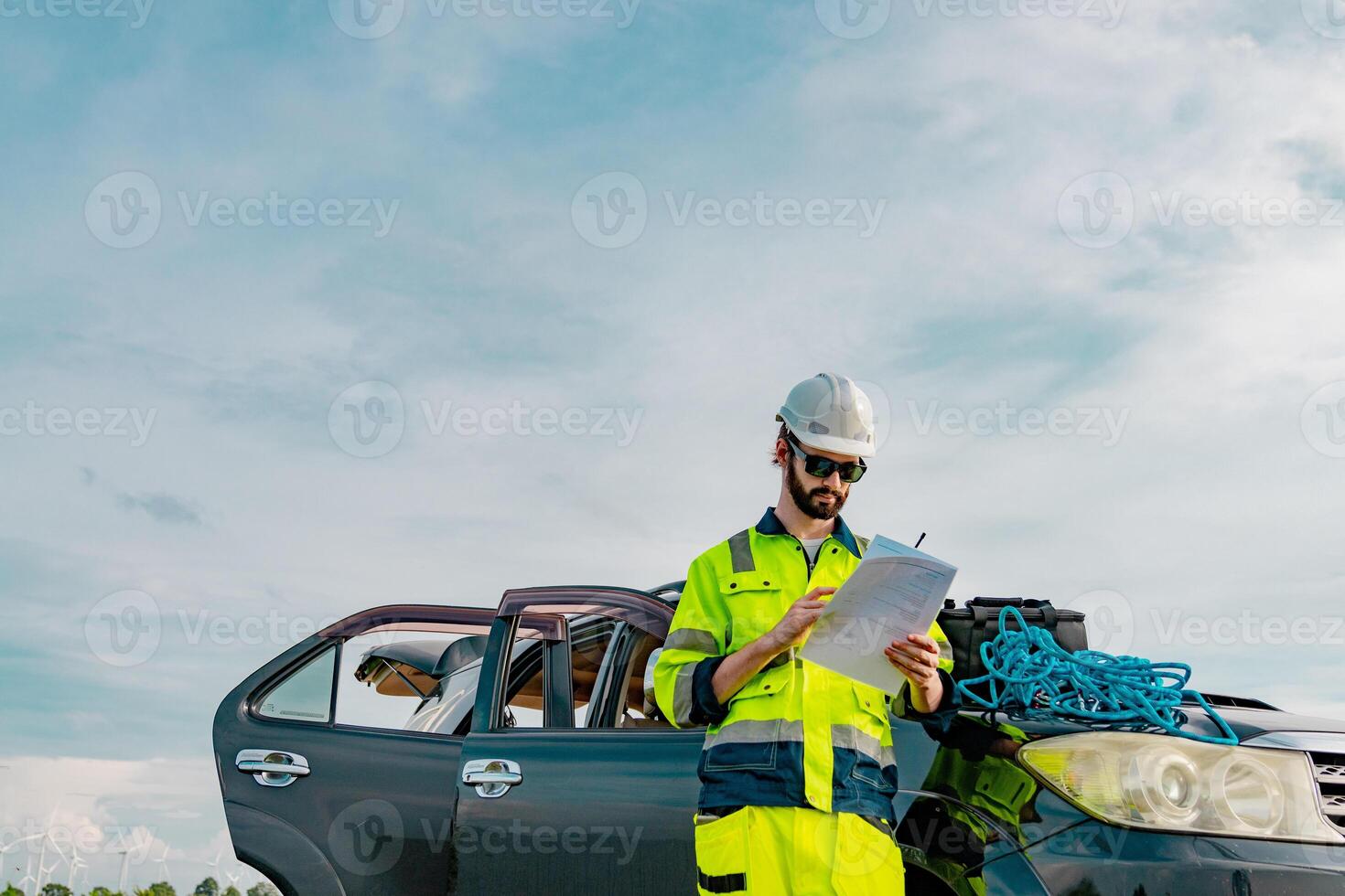 Worker in safety gear conducts inspection on vehicle amid cloudy skies photo