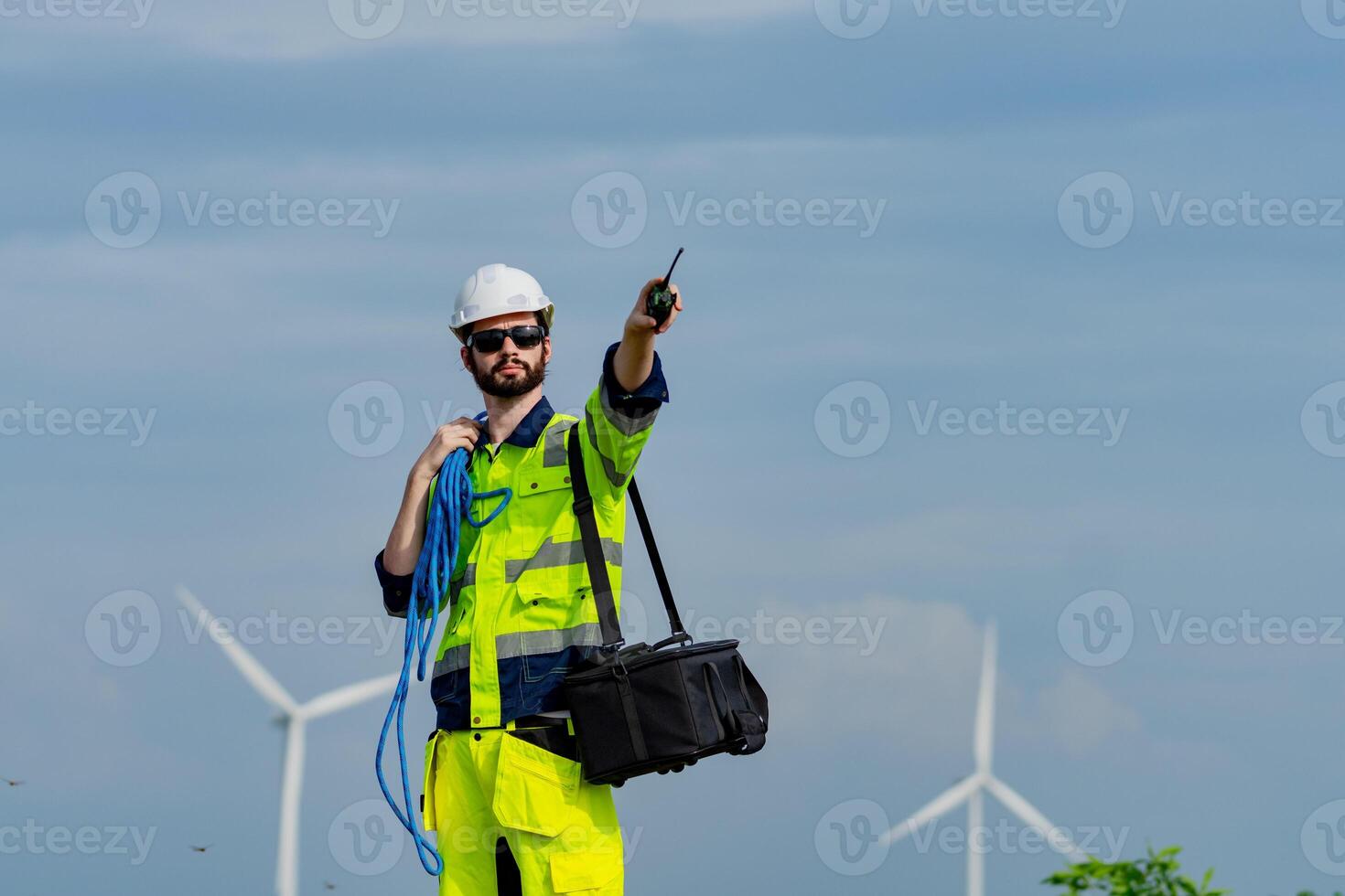 Worker in safety gear directs operations at wind farm with turbines in background during daytime photo