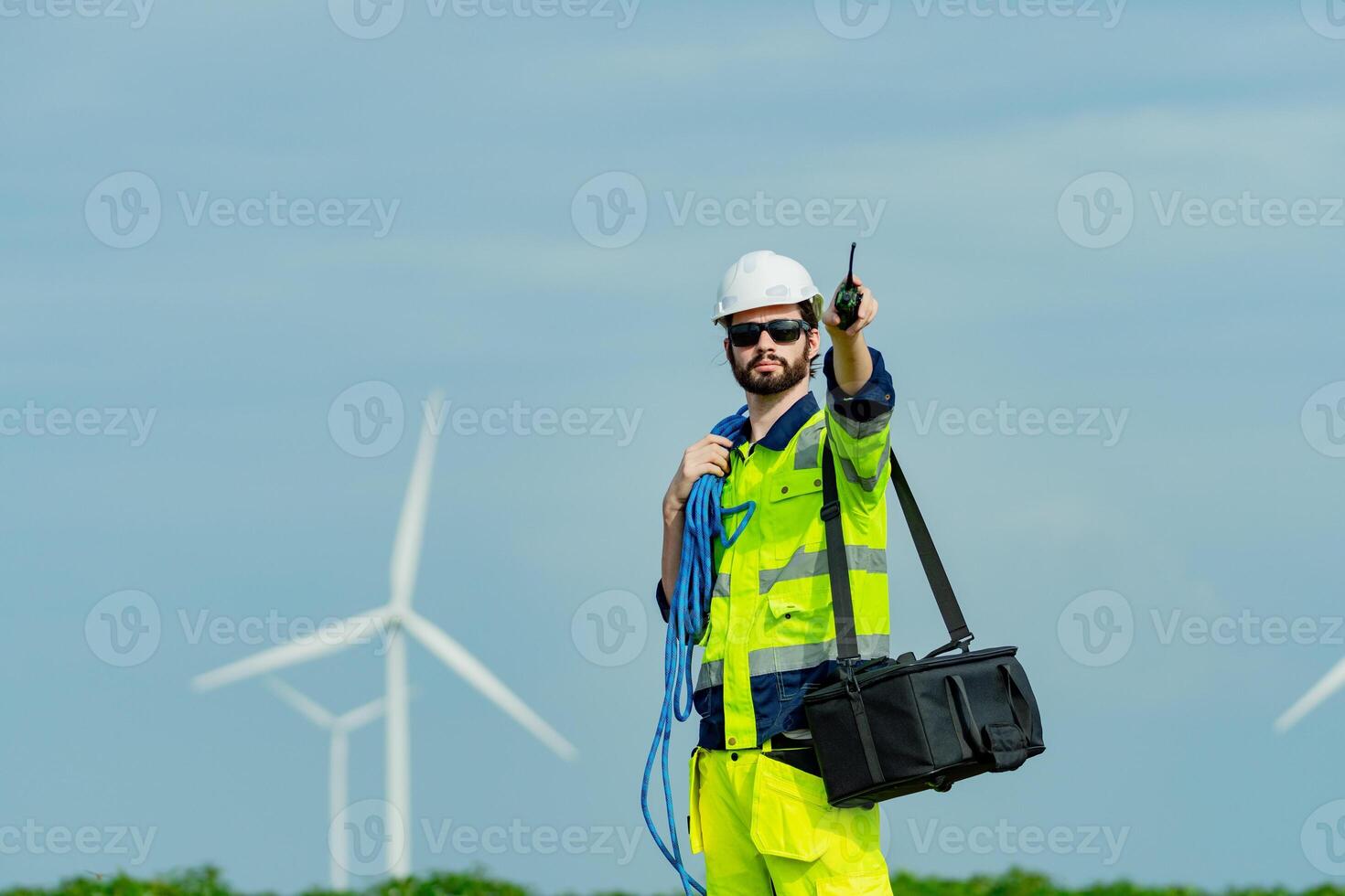 Wind turbine technician operates communication equipment while performing safety checks in bright daylight photo