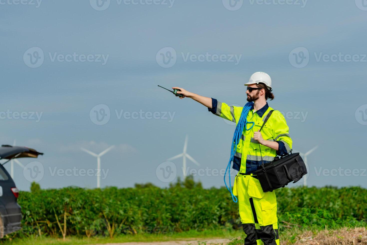 Professional technician conducts maintenance in a renewable energy field with wind turbines in the background photo