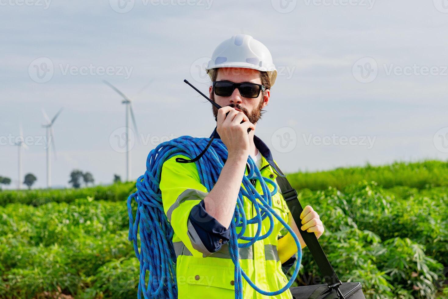 Worker communicates on radio while managing equipment near wind turbines in green field landscape photo