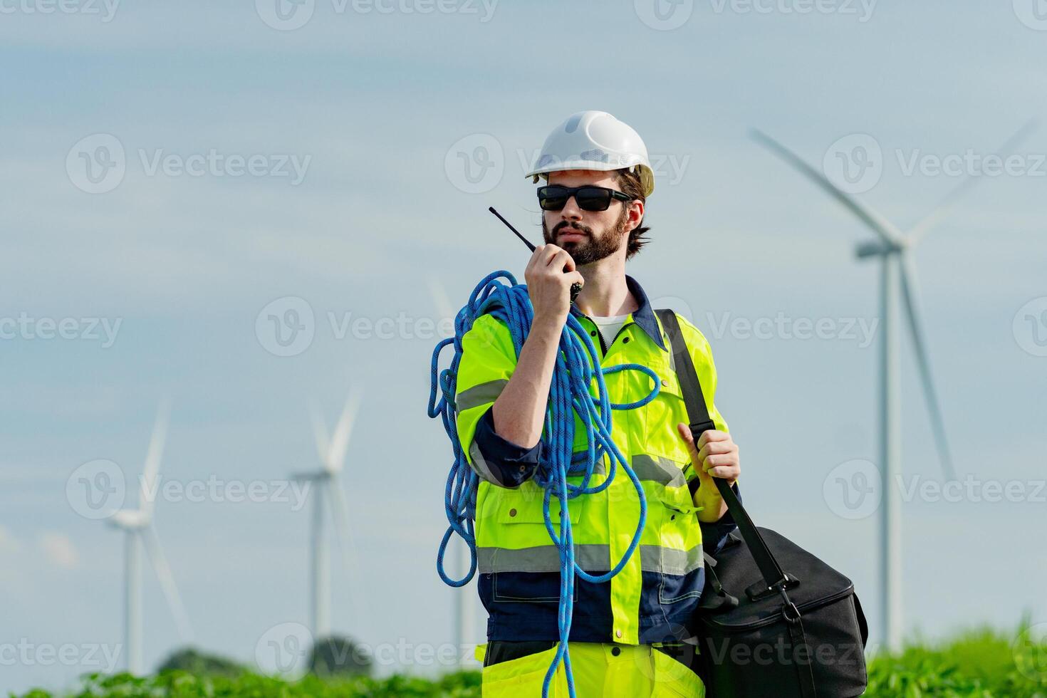 Worker in safety gear manages equipment near wind turbines during a sunny day photo