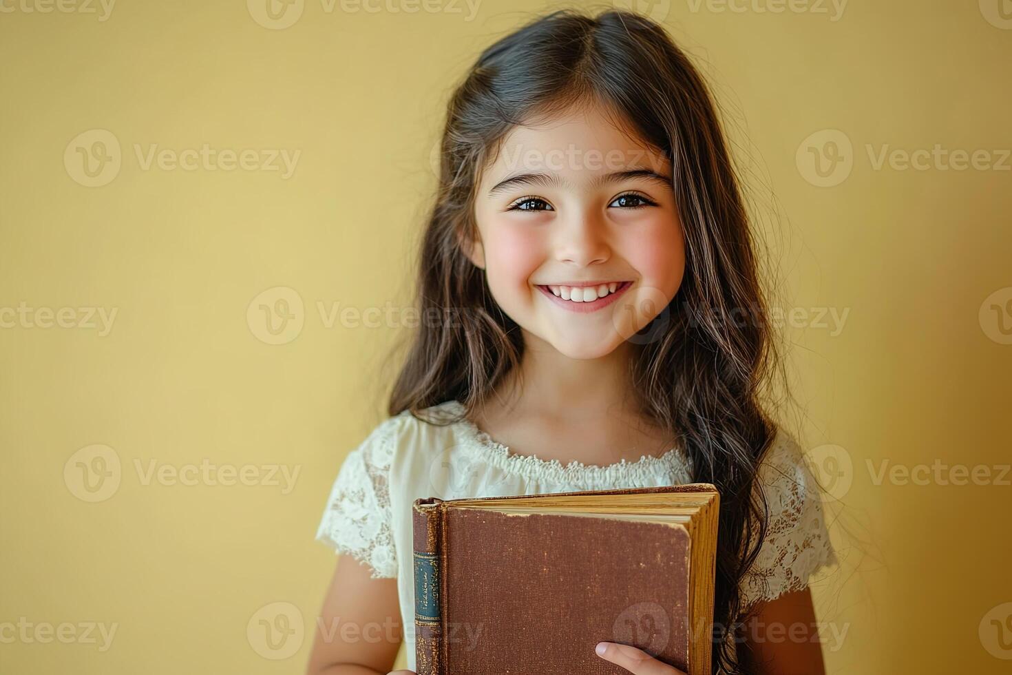 portrait of a cute smiling girl holding book on yellow background with copy space photo