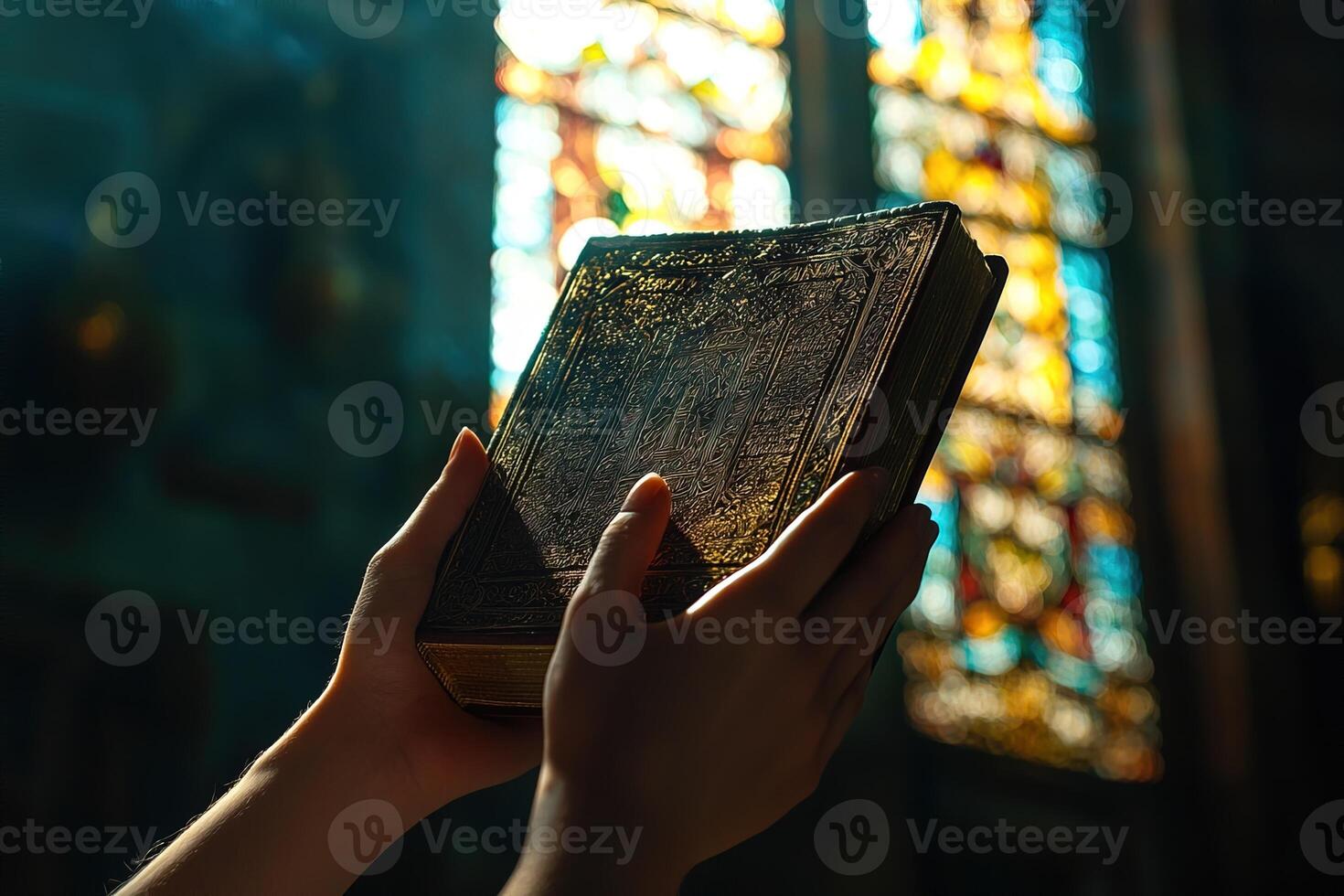 close-up of hands holding old traditional religious book, with a blurred backdrop of a stained-glass window photo