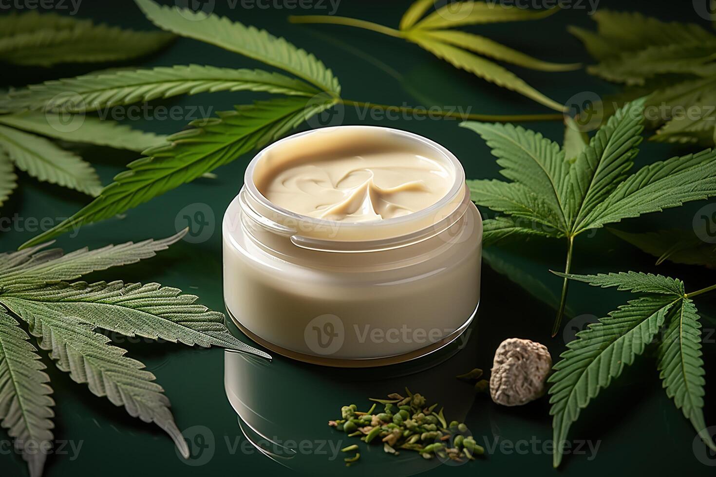 top view close-up of jar of natural organic cream surrounded by green marijuana leaves standing on dark reflective surface photo