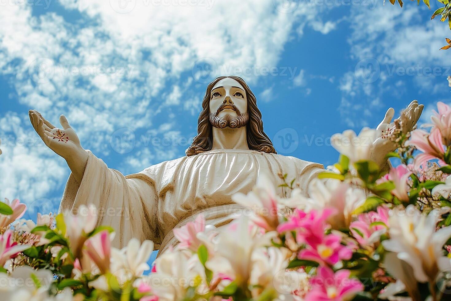 bottom view Jesus Christ statue standing with different colorful flowers around against a dramatic sky photo