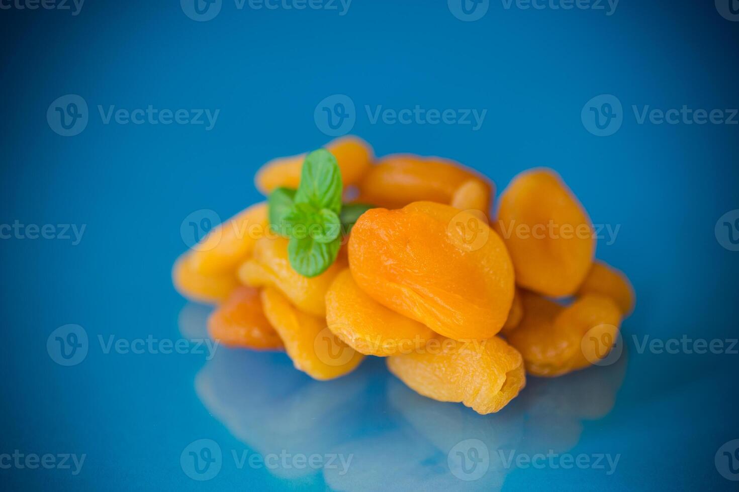 A handful of bright orange dried apricots with a sprig of mint on a blue background photo
