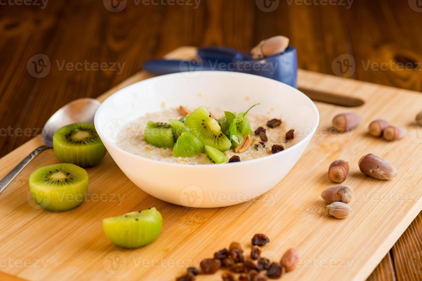 recipes with fruits.cooked oatmeal with kiwi, honey and nuts in a bowl on a wooden table photo