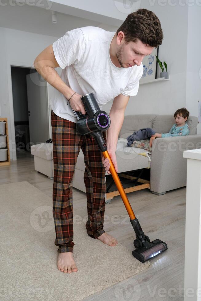 Young man using a cordless vacuum cleaner, efficient and modern home cleaning photo