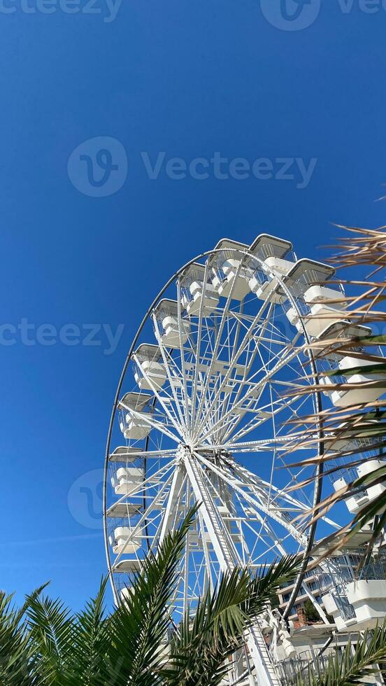 White Ferris wheel against bright blue sky, seen from below photo