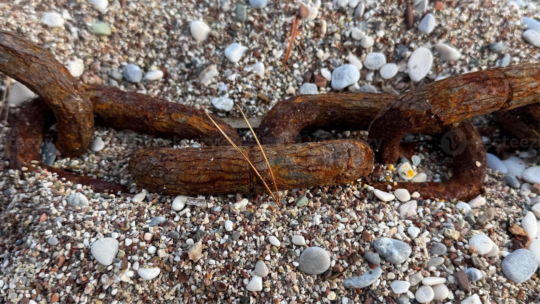 A large rusty chain on a pebble beach, washed up by a wave during a storm. High quality photos