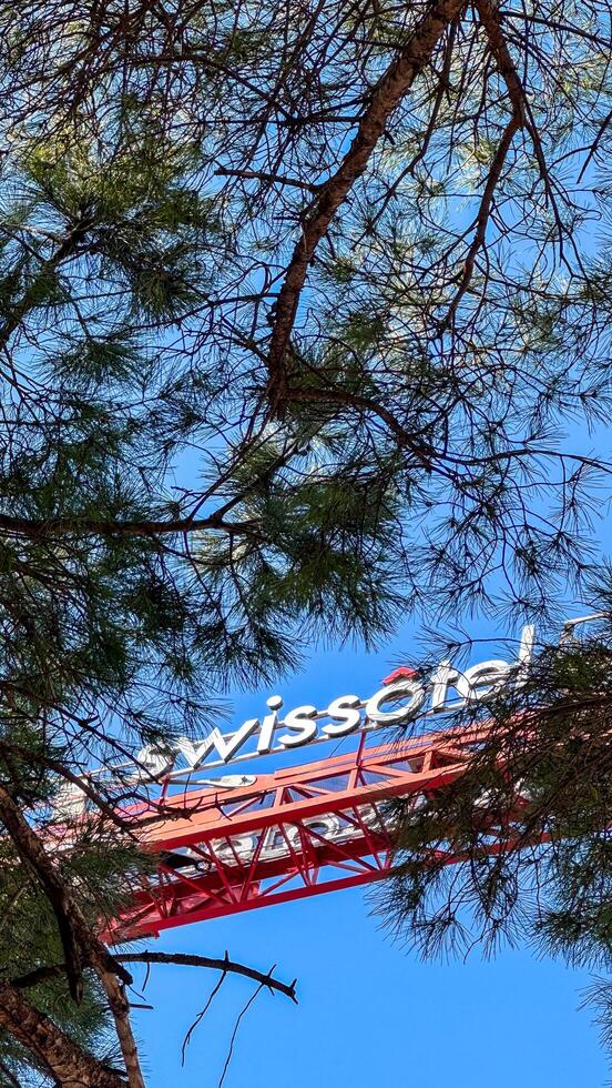 22.02.2025.Budva,Montenegro.Swissotel sign on crane boom partially visible behind tree branches, with red structure against clear blue sky. photo
