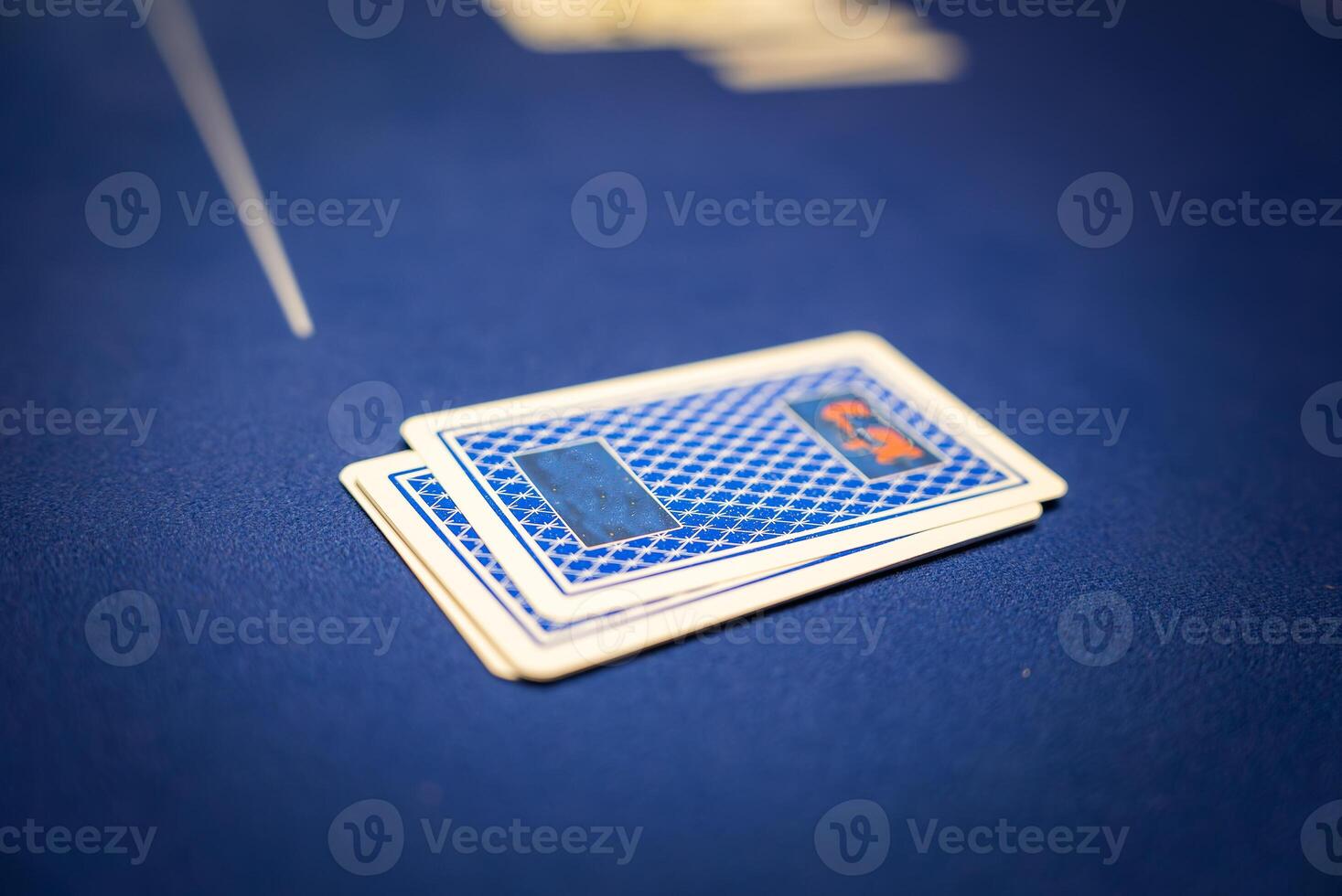 Two face down playing cards rest on a blue felt poker table with a geometric pattern. The blurred background suggests additional game elements. photo