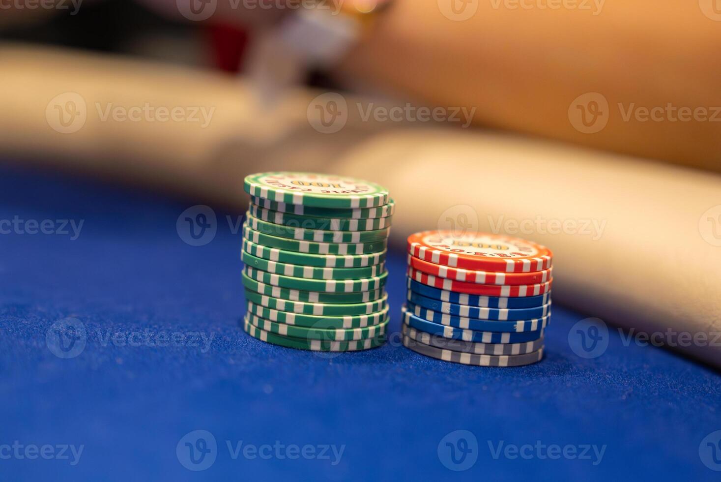 Poker chips in green, red, blue, and gray with white detailing are stacked on a blue felt table. A blurred arm suggests an active game in progress. photo