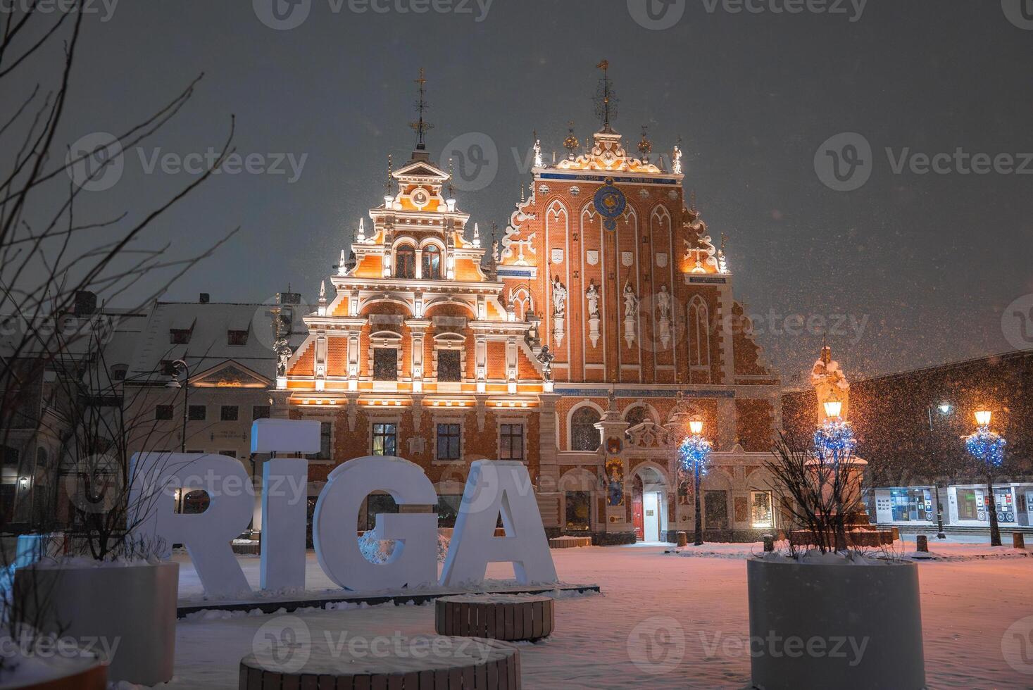 The House of the Blackheads in Riga, Latvia, glows with warm lights. Snowfall, blue lit trees, and large RIGA letters create a festive atmosphere. photo