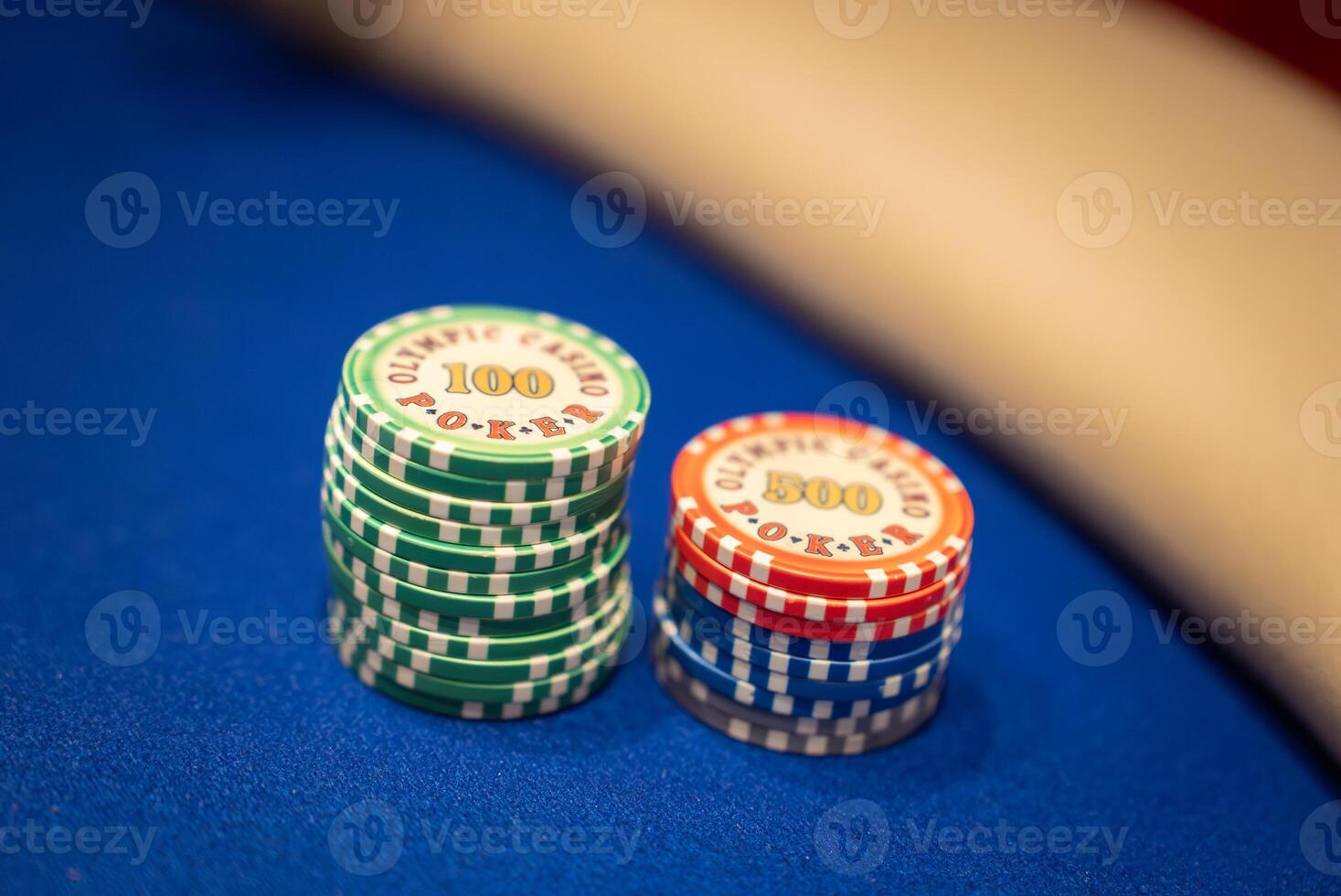 Green and red poker chips labeled Olympic Casino Poker are neatly stacked on a blue felt table. A beige surface is visible in the background. photo