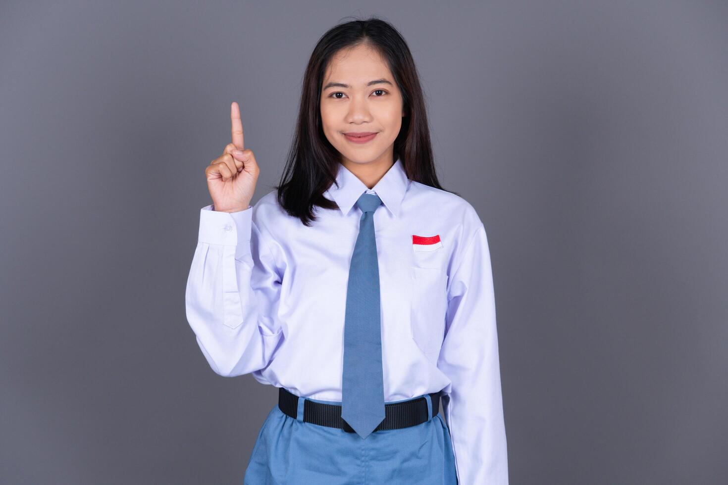 Indonesian Girl High School Student in Uniform Smiling While Pointing Finger Isolated Background photo