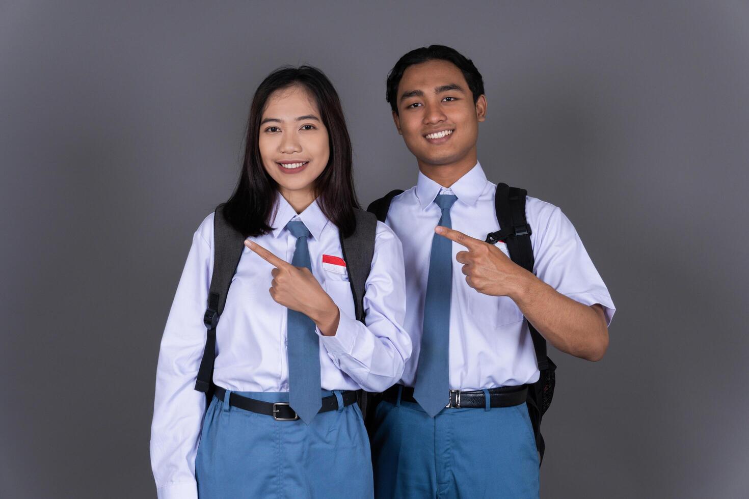 Indonesian Male and Female High School Student in Uniform Smiling While Pointing Finger Isolated Background photo