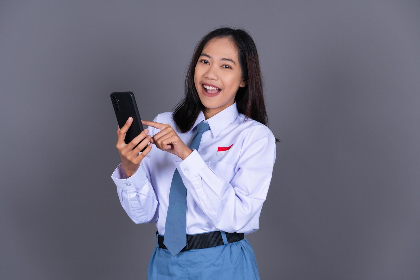 Indonesian Female High School Student in Uniform Smiling While Holding Phone photo
