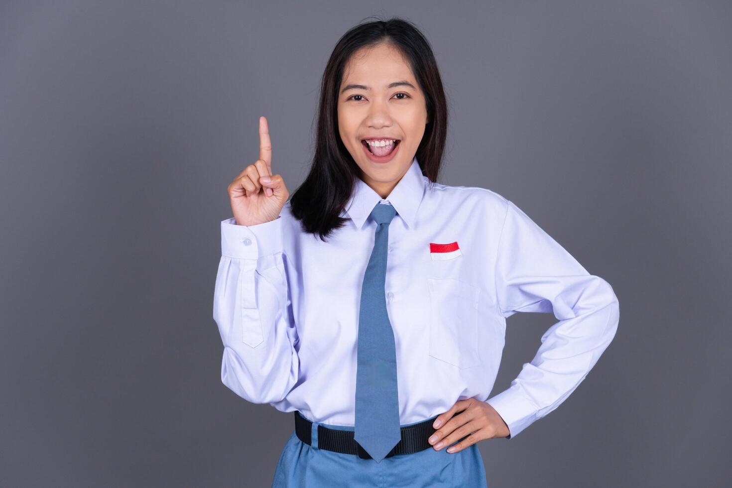 Indonesian Female High School Student in Uniform Smiling While Pointing Finger Isolated Background photo