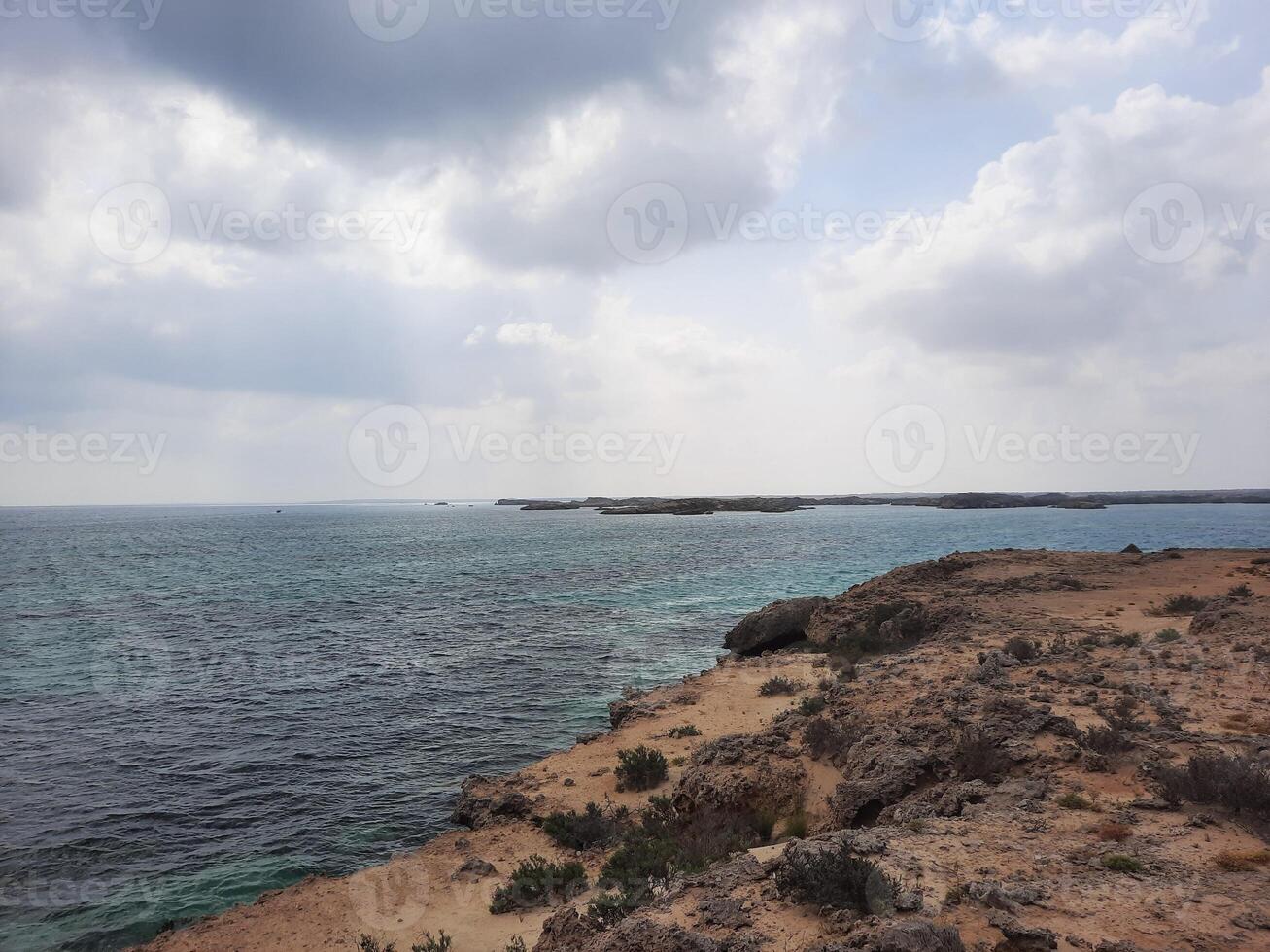 The daytime view of Al Farasan Islands in Jazan, Saudi Arabia, is stunning. The deep blue water, rocky formations, and dark clouds create a beautiful scene. photo