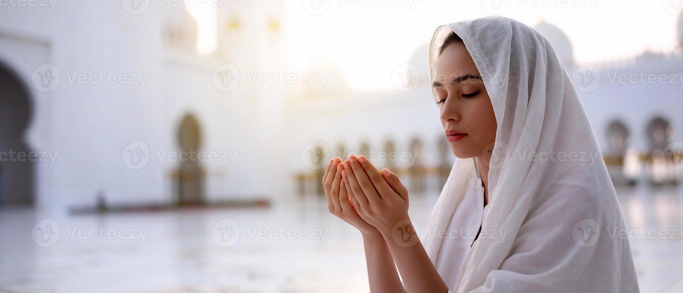 Muslim lady in traditional white attire praying with raised hands outside a mosque. Spiritual connection in Islam photo
