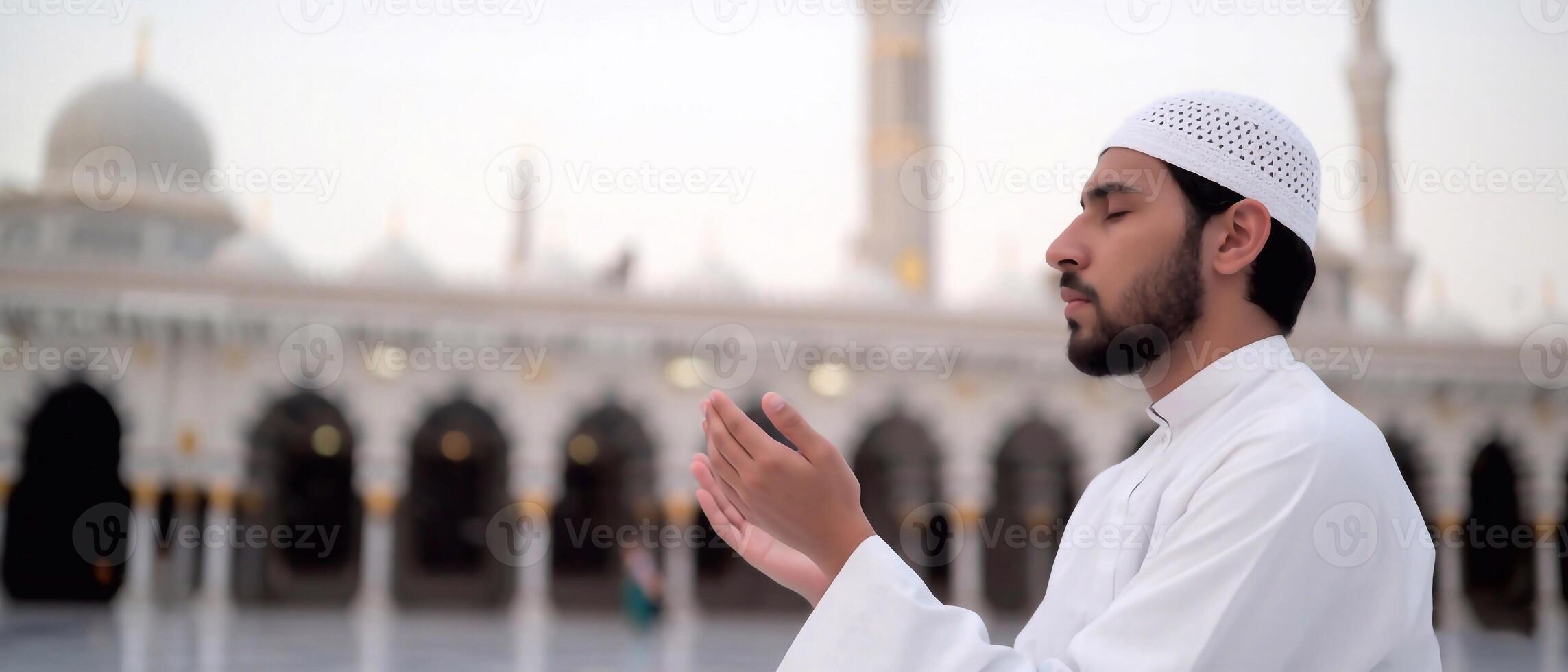 Middle Eastern man in white thobe performing Islamic prayer in front of a grand mosque. Faith and Ramadan spirituality photo