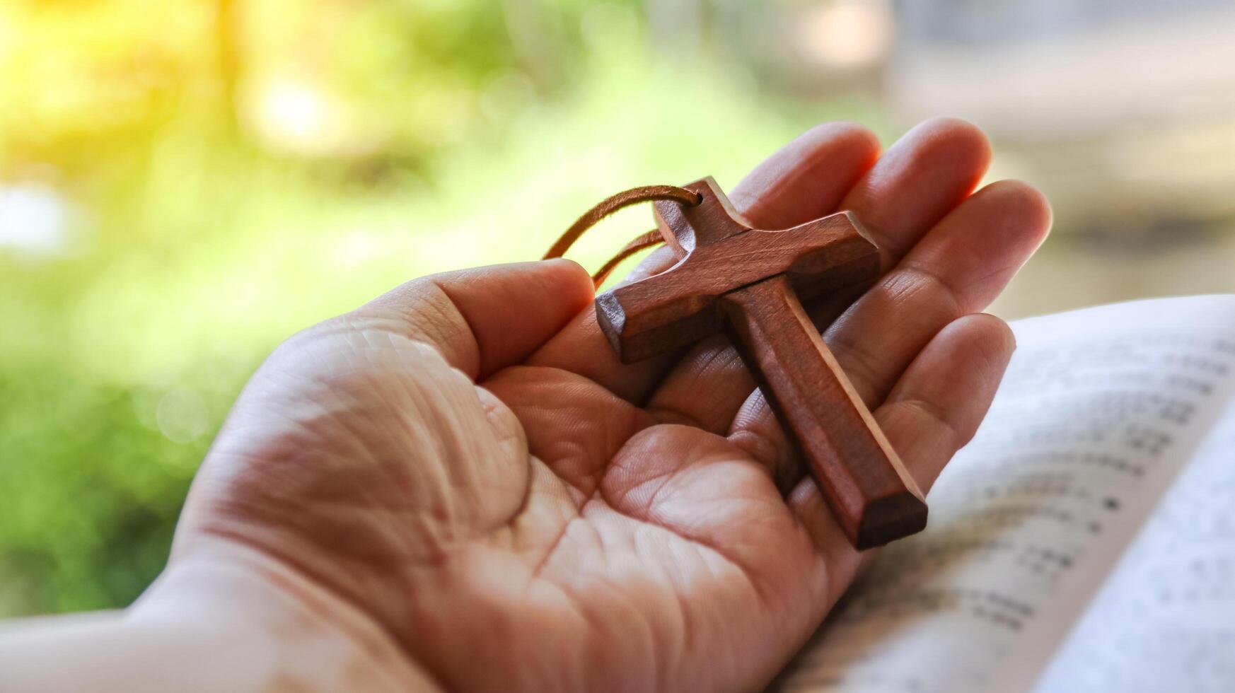 Dark brown wooden cross on a hand symbolizing the spread of Jesus Christs love among Christians reflecting faith devotion and the importance of Christian teachings. photo