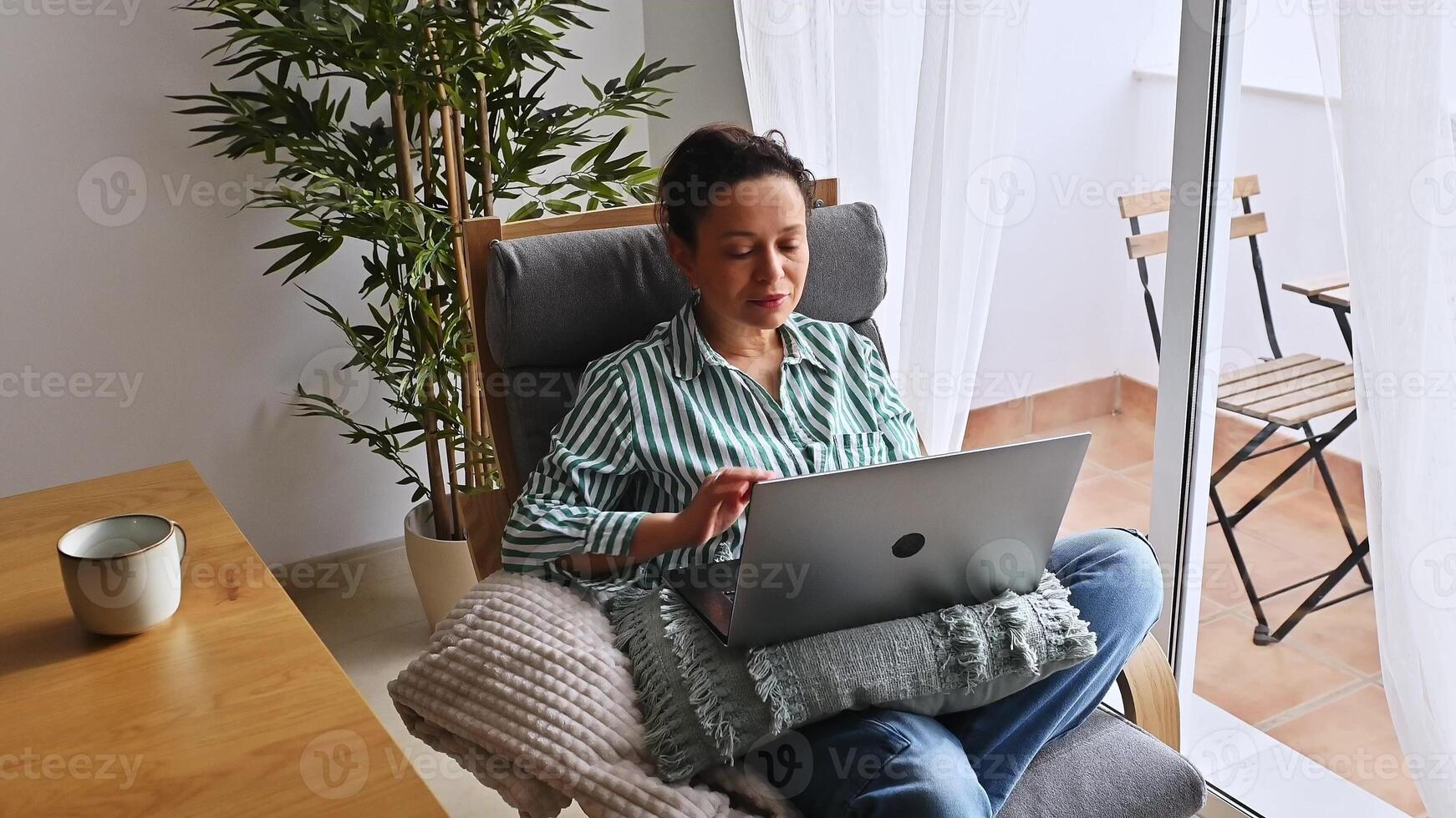 A young woman enjoys a serene moment working remotely from a cozy home office setup near countryside views, combining leisure with productivity. photo