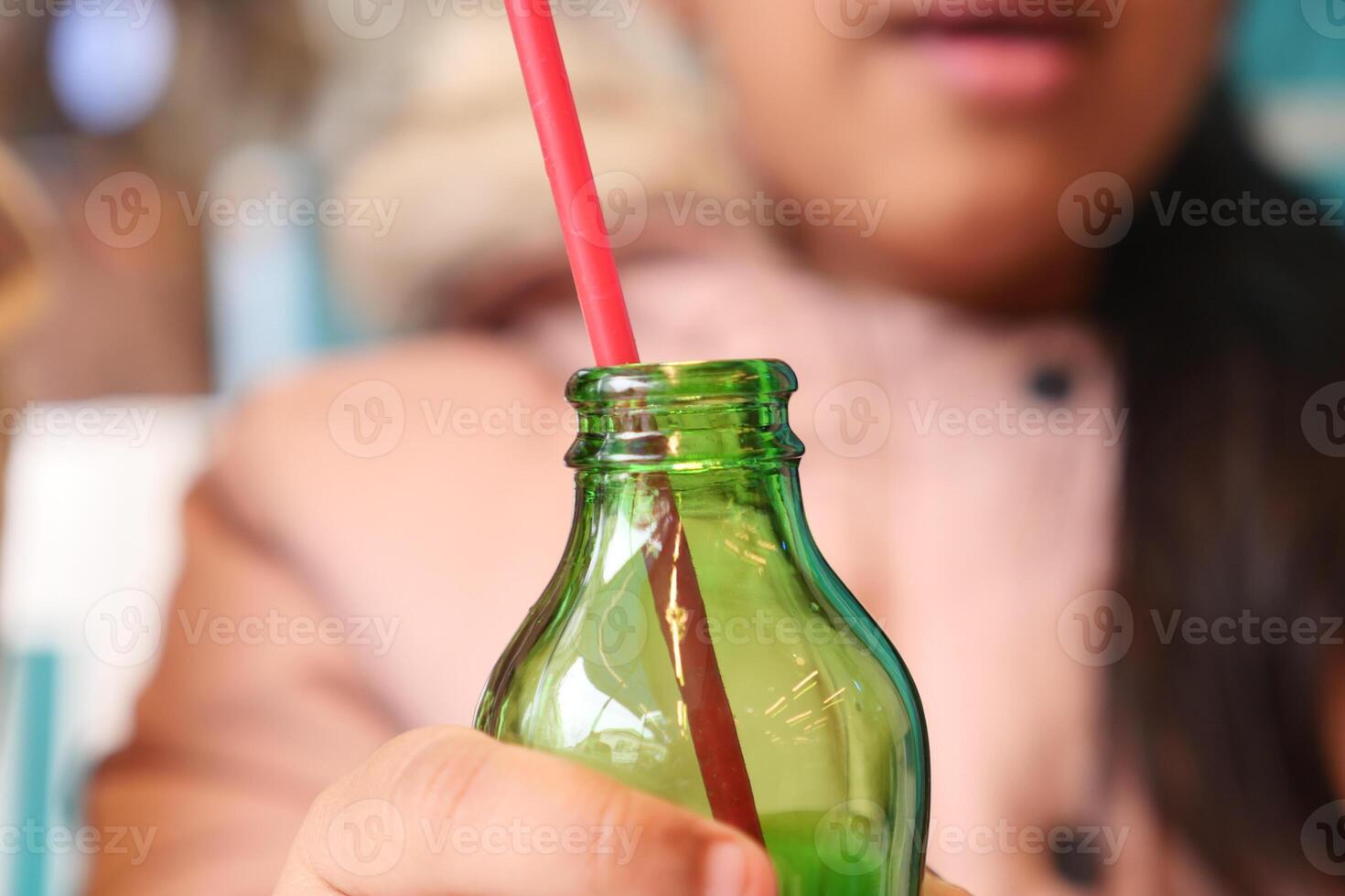 A Child Hand holding a green glass bottle with a straw in a cafe photo