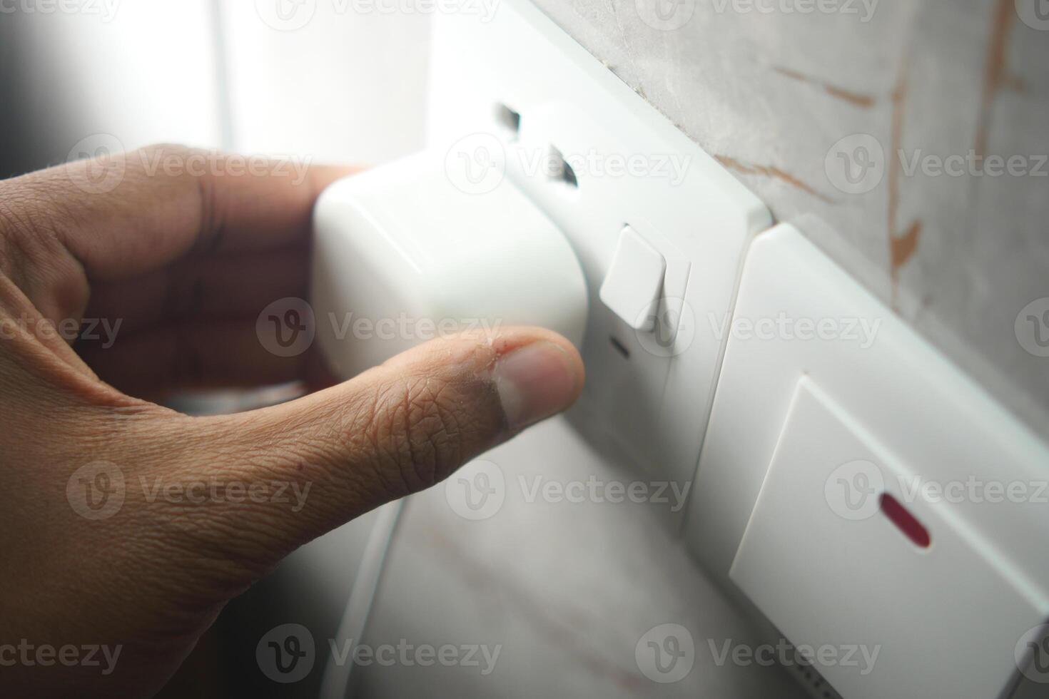 Hand plugging in a charger into a power outlet at home photo