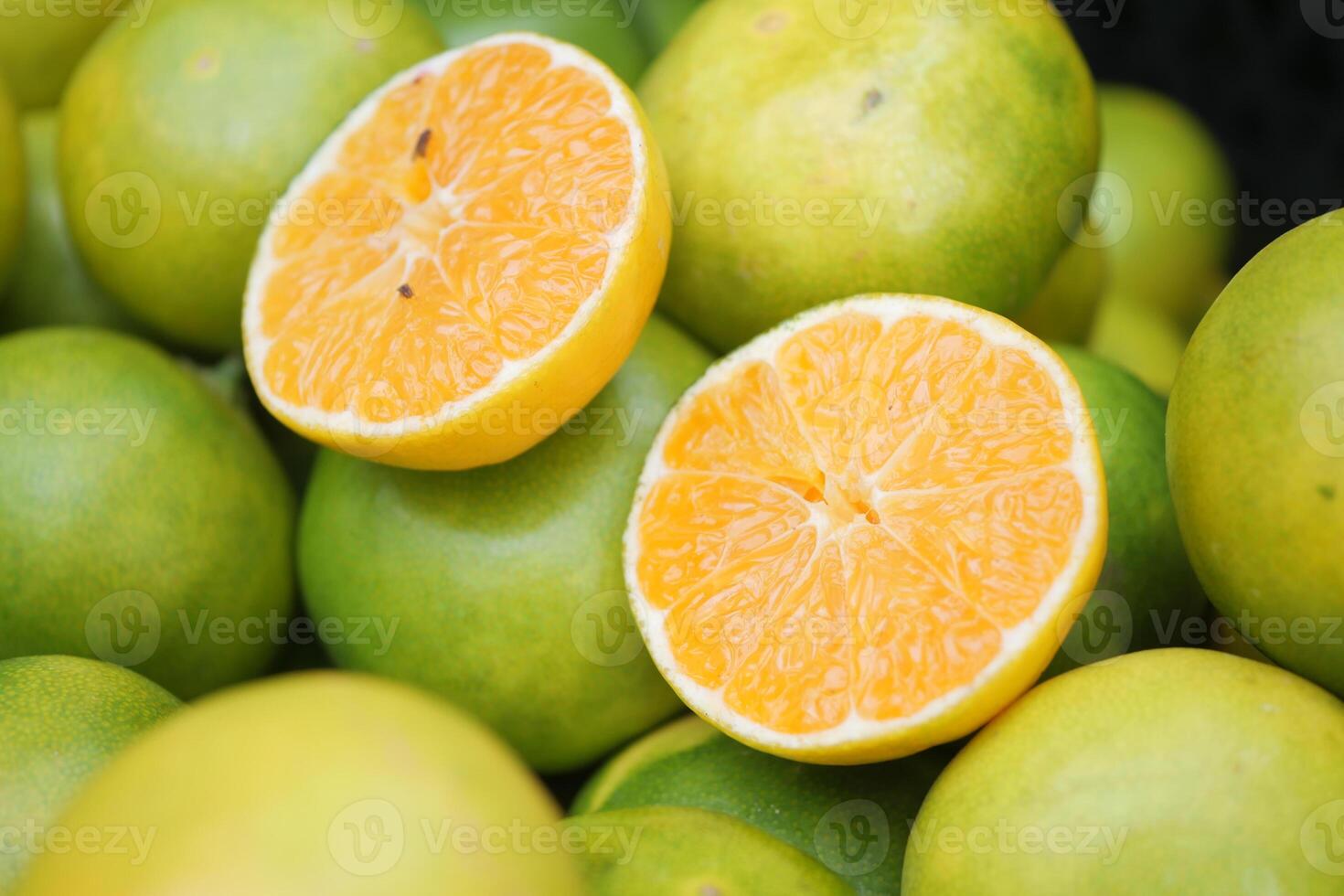 Halved oranges sit among whole green oranges at a bustling market photo