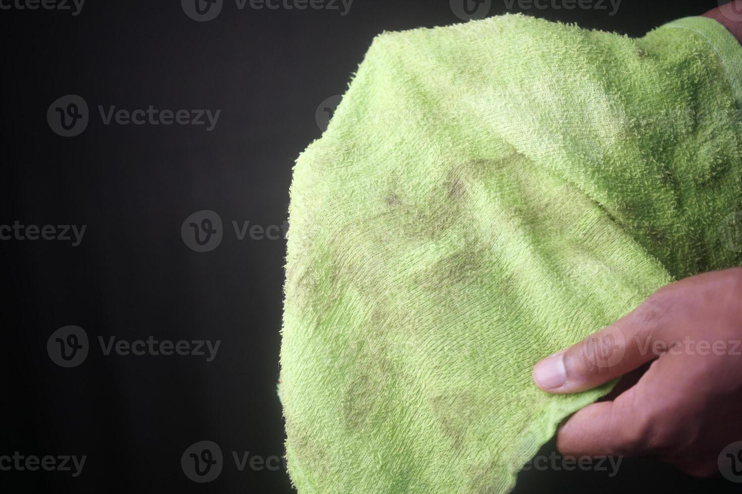 Dirty green towel held in hand against dark background photo