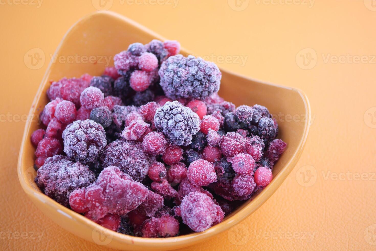 Frozen mixed berries in a bowl on a bright orange surface photo